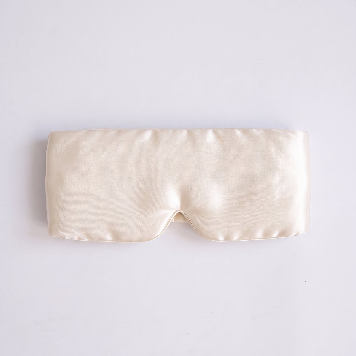 A cream-colored satin sleep mask laid flat on a light gray background.