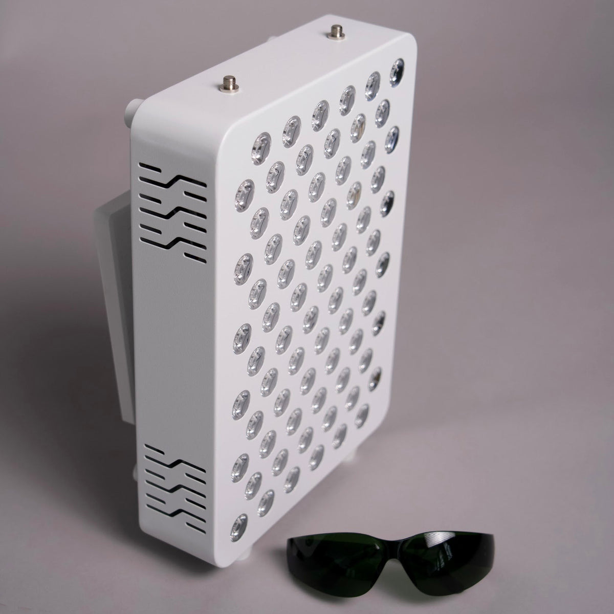 A white rectangular LED light panel with multiple circular light elements on the front, shown standing upright on a gray background with a pair of dark sunglasses placed in front.