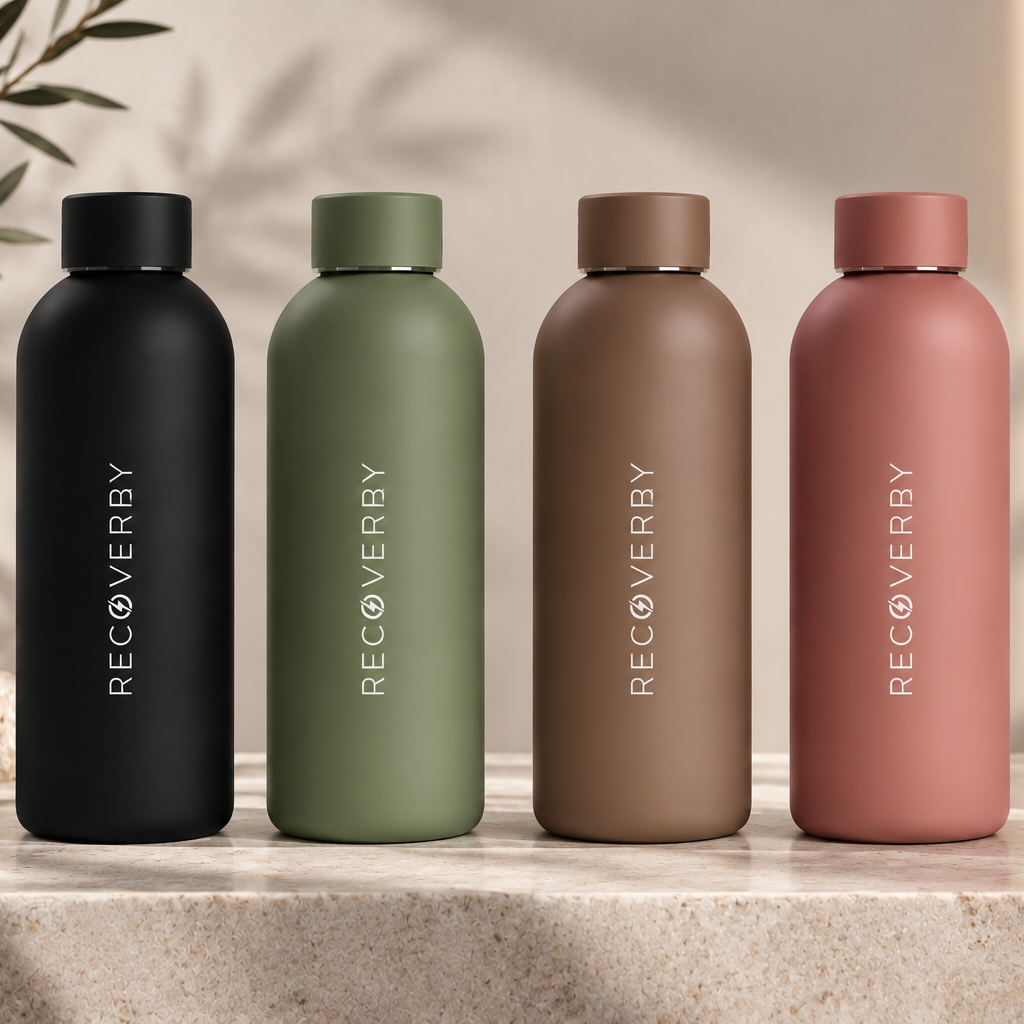 Four matte water bottles in black, olive green, taupe brown, and dusty rose, lined up on a stone surface with a warm neutral background and decorative props.